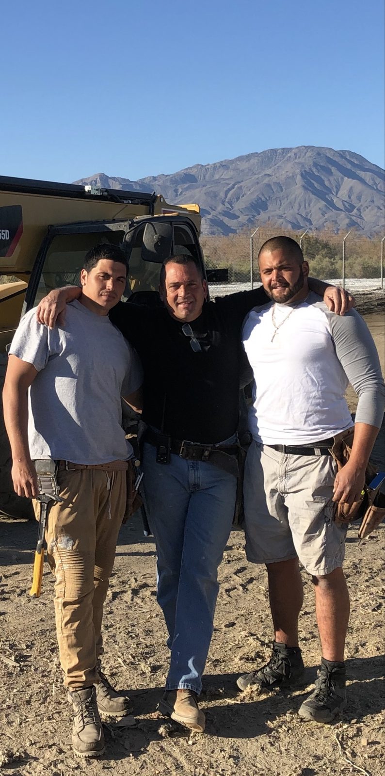 Three crew members posing in front of heavy equipment on a job site