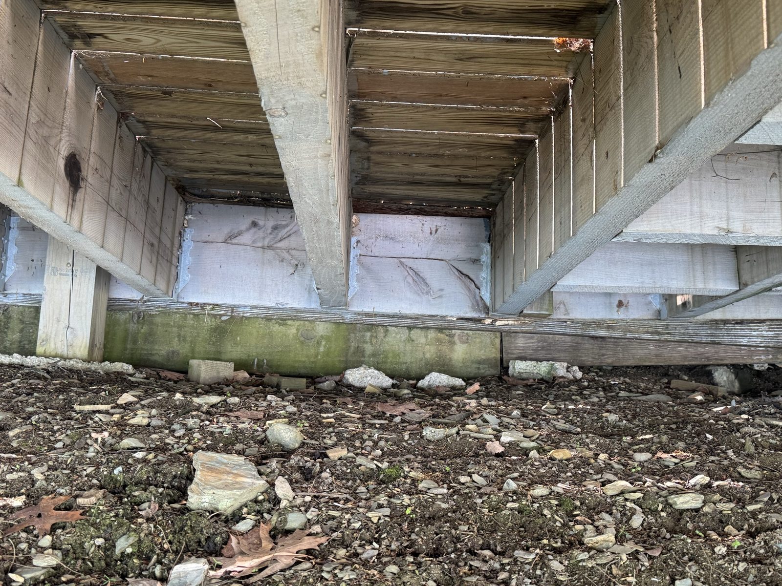 Old rotted lakeside walkway underside showing decayed support beams before replacement
